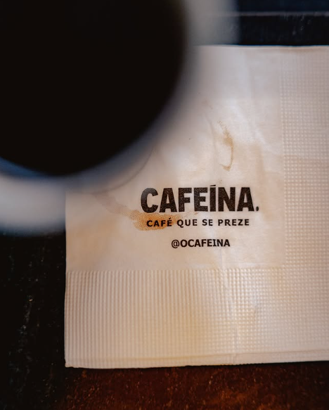 Detalhe do guardanapo da Cafeína sobre a mesa, ao lado de uma xícara